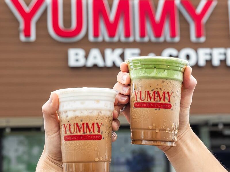 Two Yummy iced coffee drinks held up in front of the storefront sign